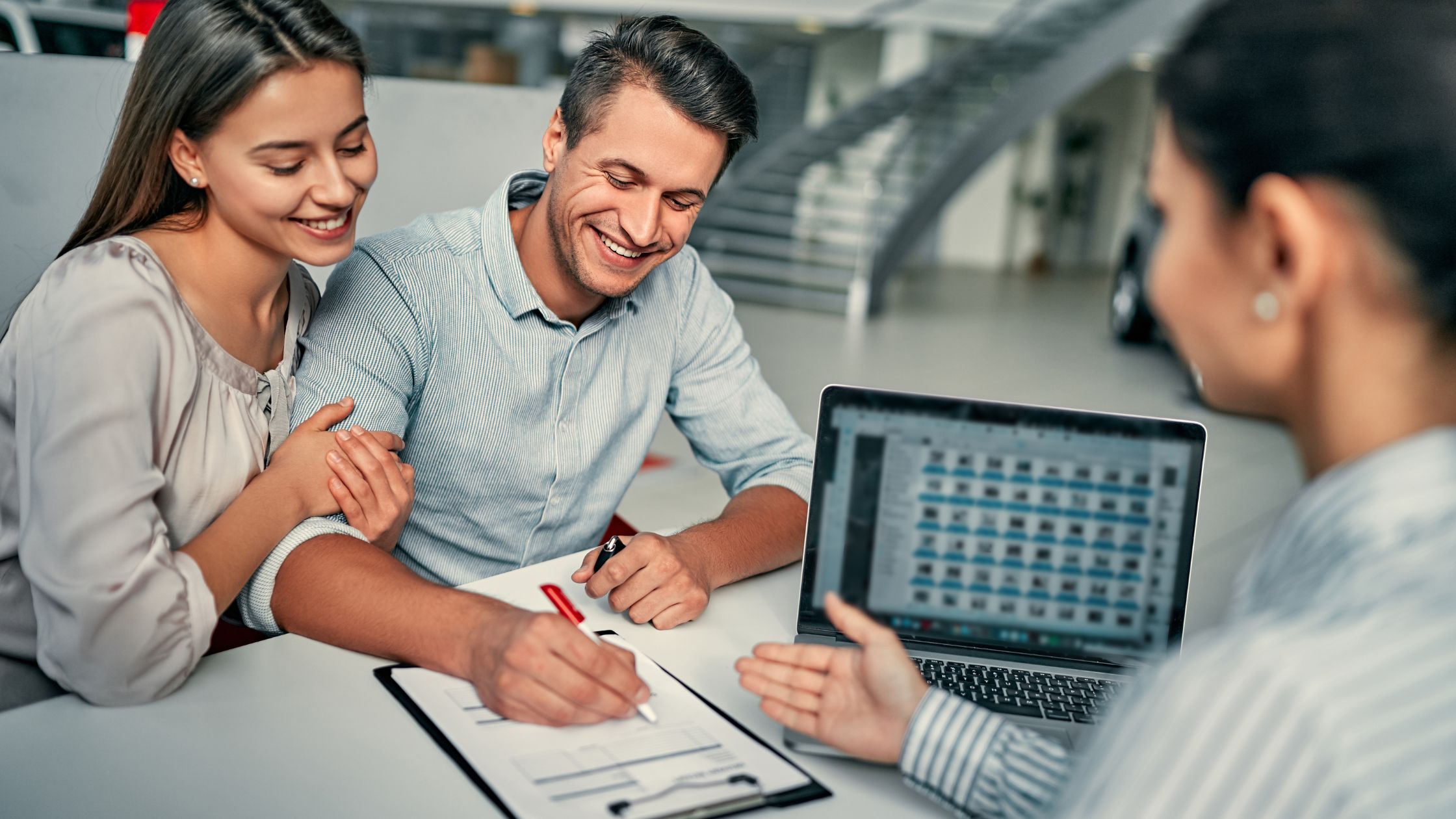 man and woman signing paperwork at car dealership